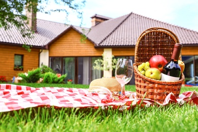 Picnic basket with fruits and bottle of wine on checkered blanket in garden