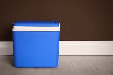 Photo of Closed blue plastic cool box near brown wall. Space for text
