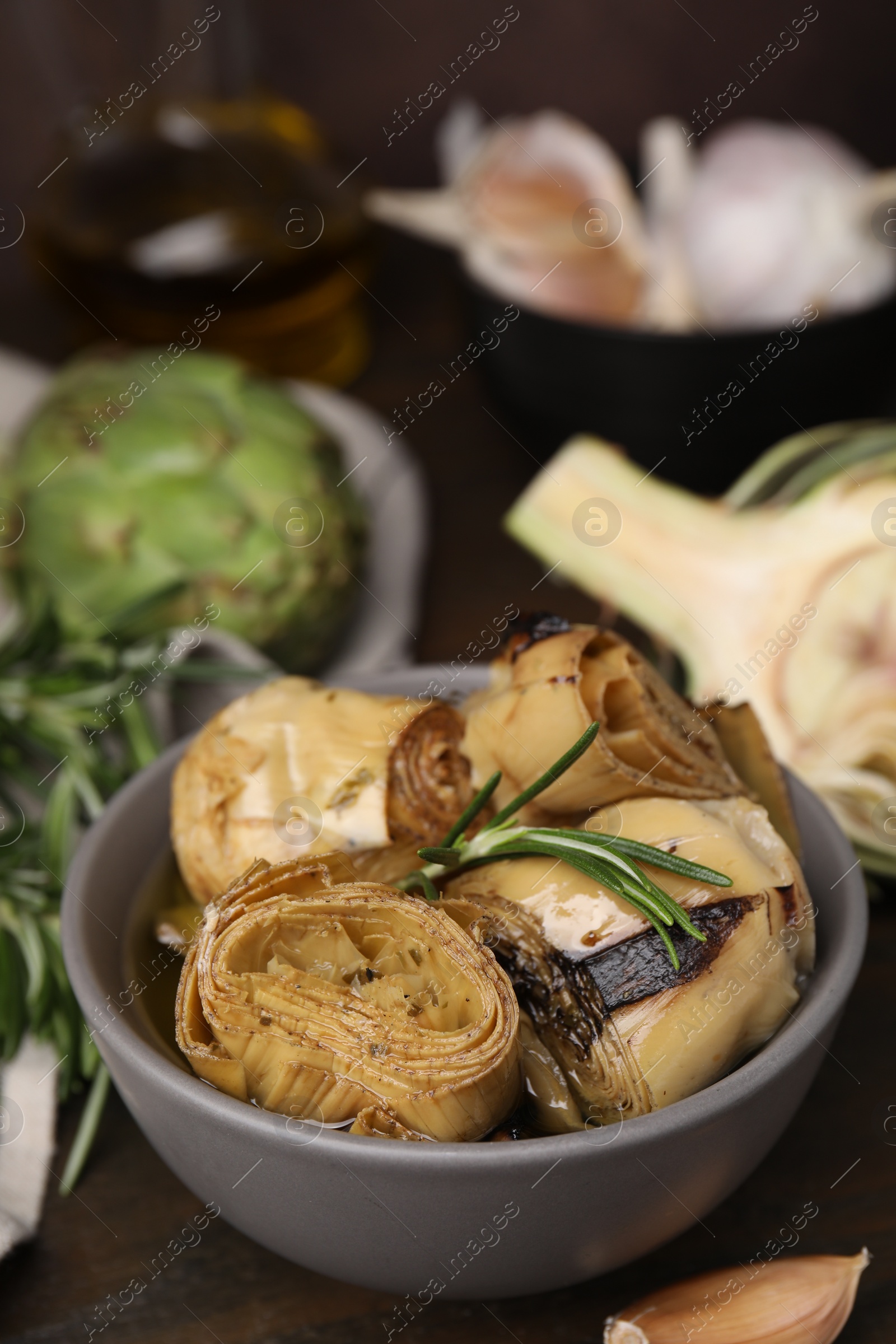 Photo of Bowl with delicious artichokes pickled in olive oil on wooden table, closeup