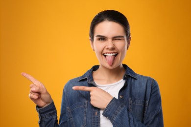 Photo of Happy young woman showing her tongue and pointing on yellow background