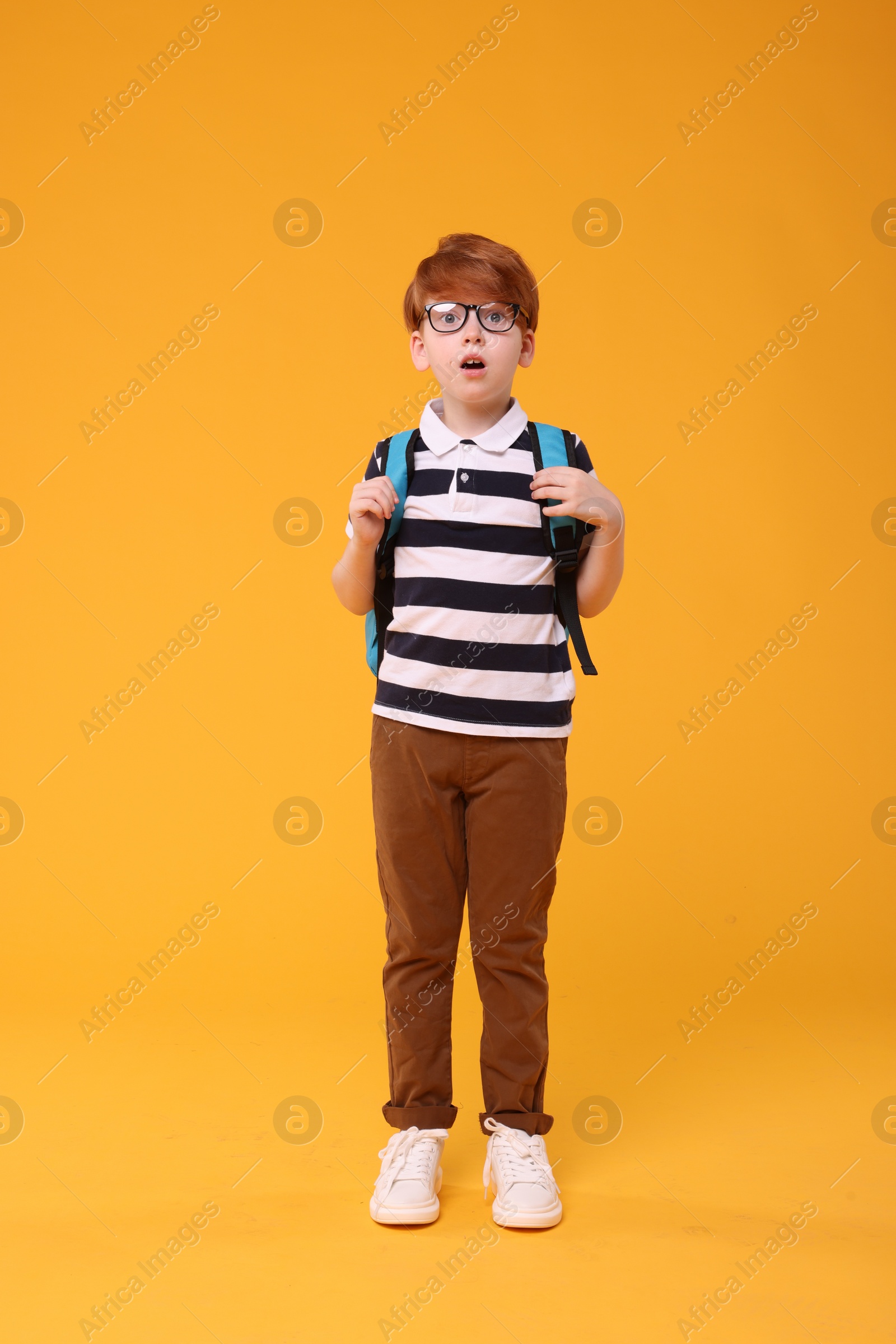 Photo of Surprised schoolboy in glasses on orange background