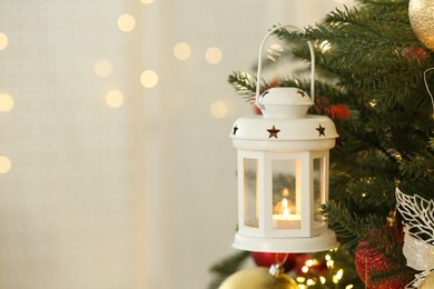 Christmas lantern with burning candle on fir tree indoors, closeup. Space for text
