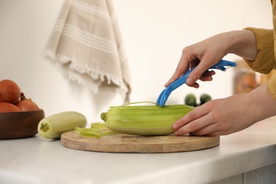 Woman peeling zucchini at kitchen counter, closeup. Preparing vegetable