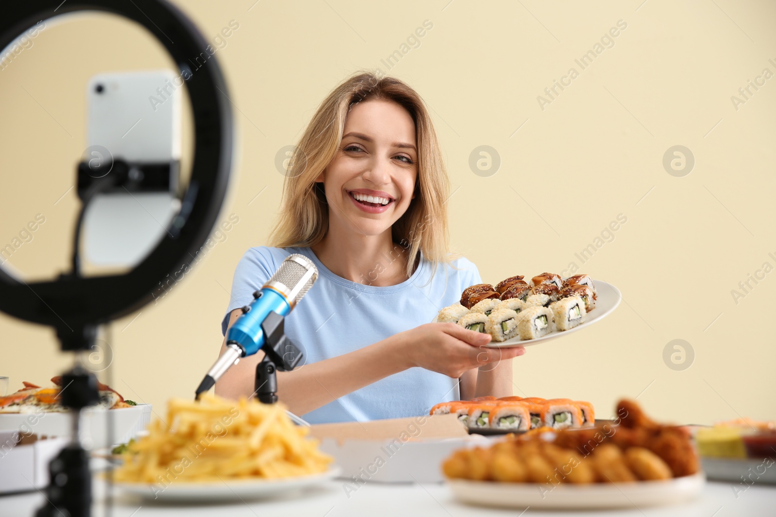 Photo of Food blogger recording eating show on smartphone camera against light background. Mukbang vlog