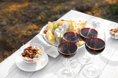 Red wine and snacks served for picnic on white wooden table outdoors