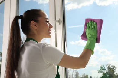 Photo of Happy young woman cleaning window glass with rag indoors