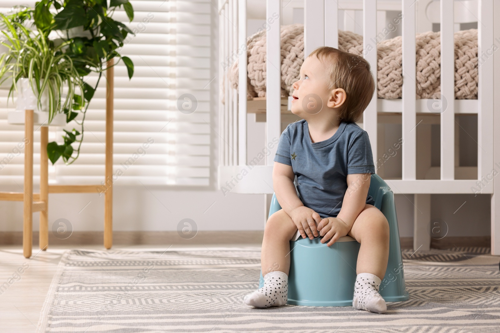 Photo of Little child sitting on plastic baby potty indoors. Space for text