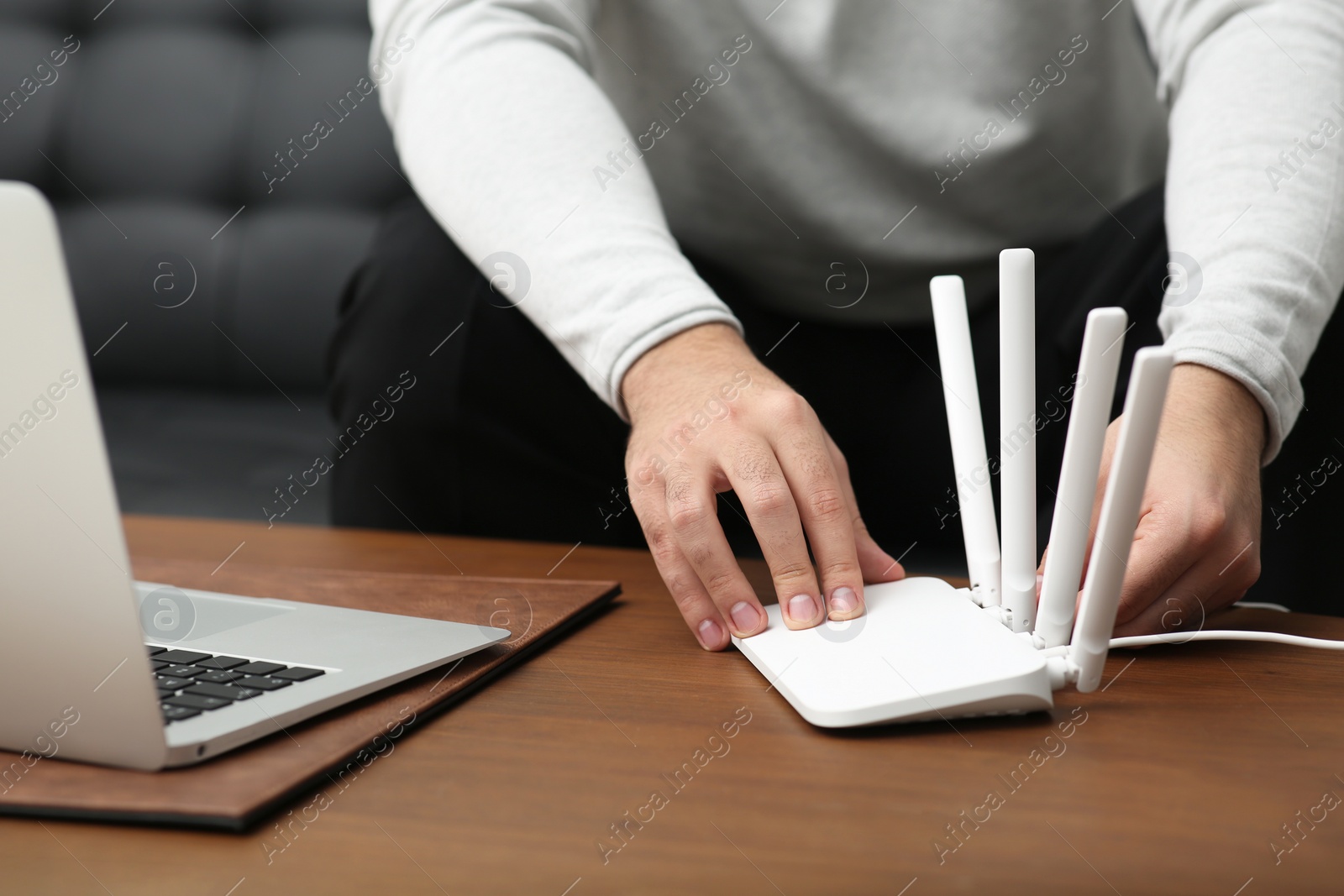 Photo of Man inserting cable into Wi-Fi router at wooden table indoors, closeup