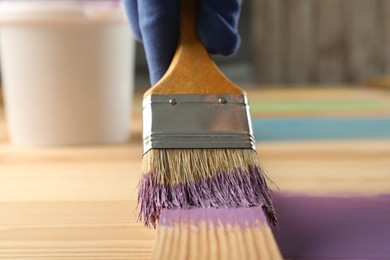 Worker applying violet paint onto wooden surface, closeup