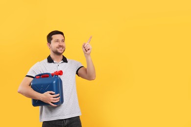 Photo of Man holding blue canister and pointing at something on orange background. Space for text