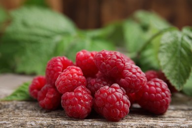 Photo of Fresh ripe raspberries and green leaves on wooden table, closeup