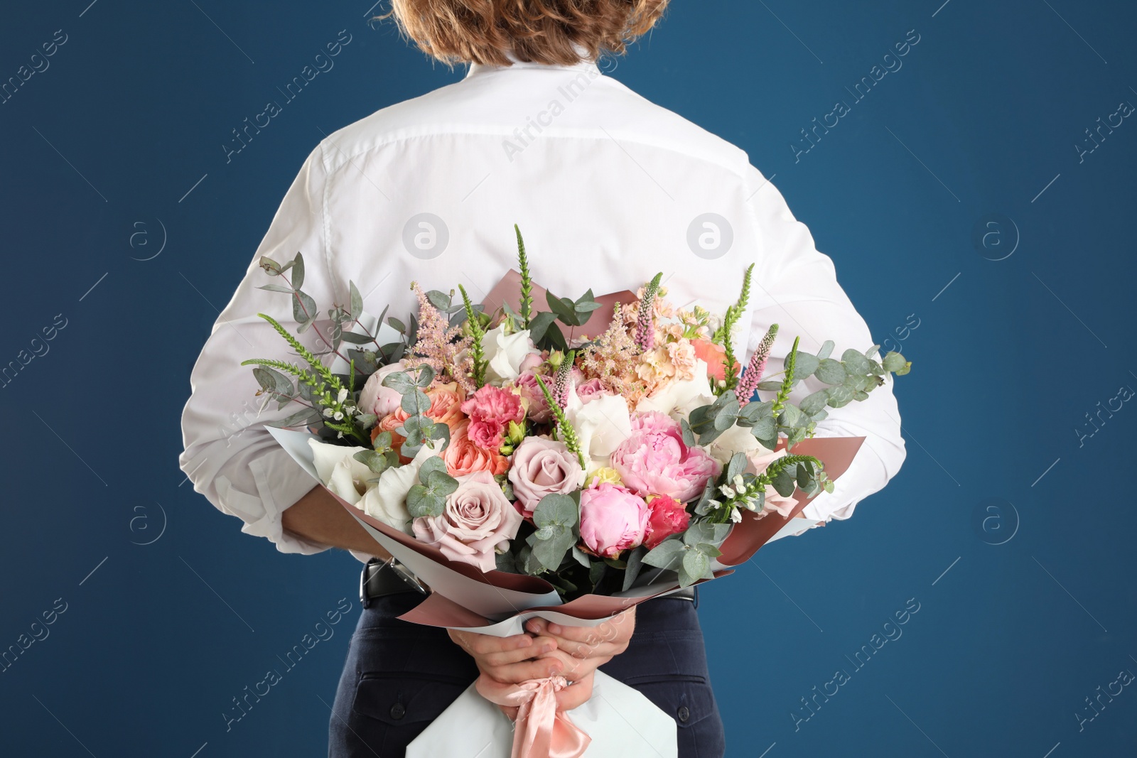 Photo of Man hiding beautiful flower bouquet behind his back on blue background