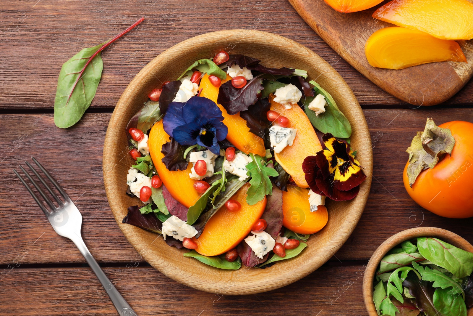 Photo of Delicious persimmon salad with cheese and pomegranate served on wooden table, flat lay