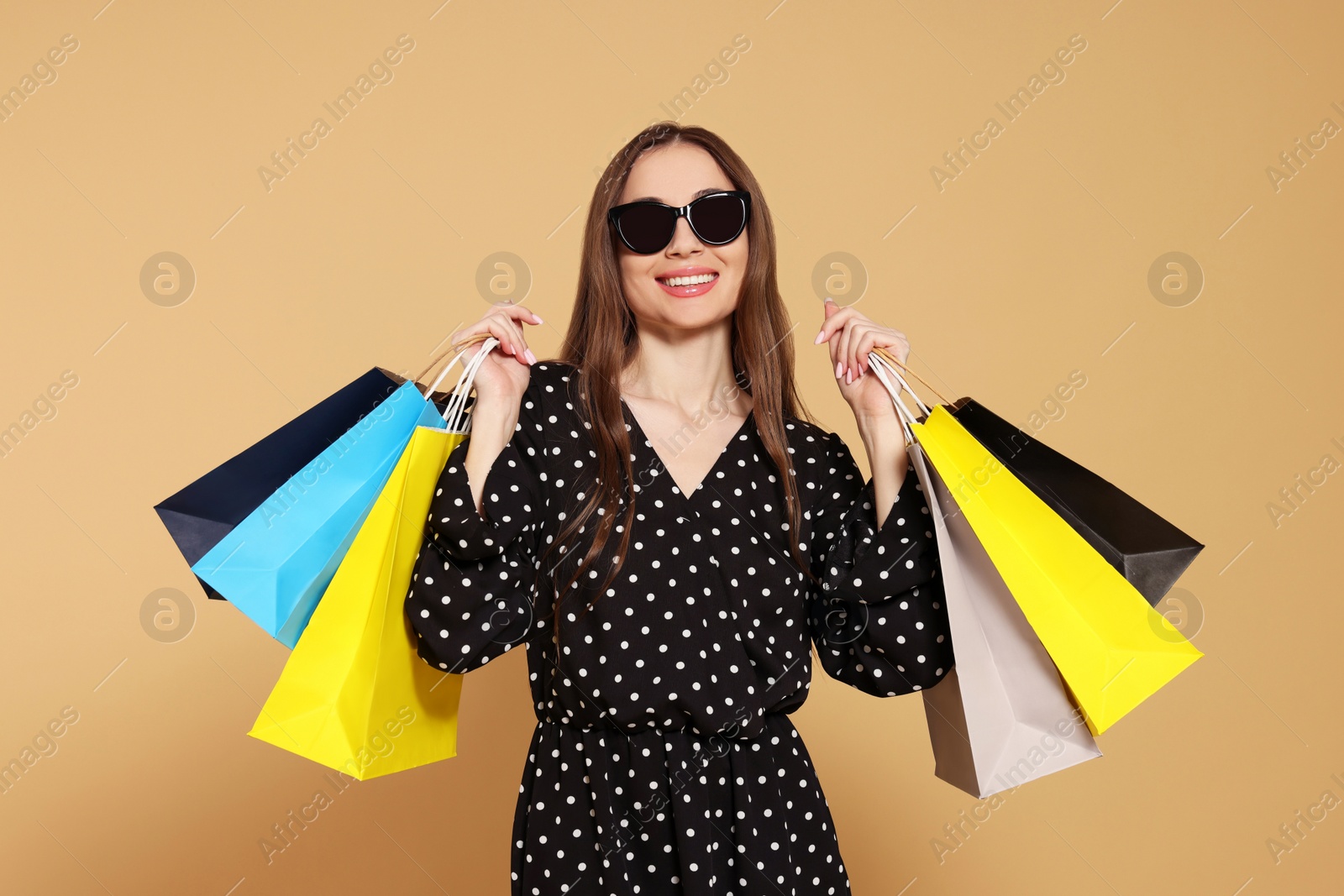 Photo of Stylish young woman in sunglasses with shopping bags on beige background