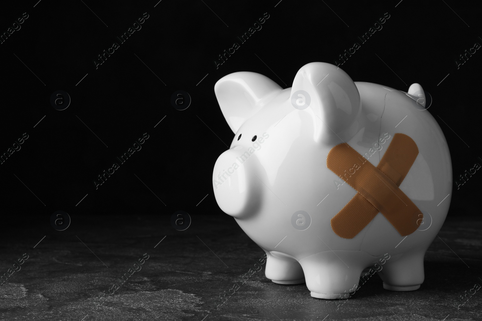 Photo of Piggy bank with sticking plasters on grey stone table. Space for text