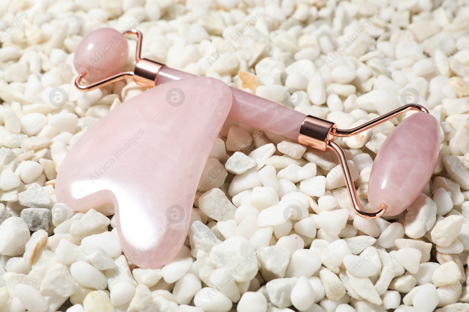 Photo of Quartz gua sha tool and face roller on white stones, closeup