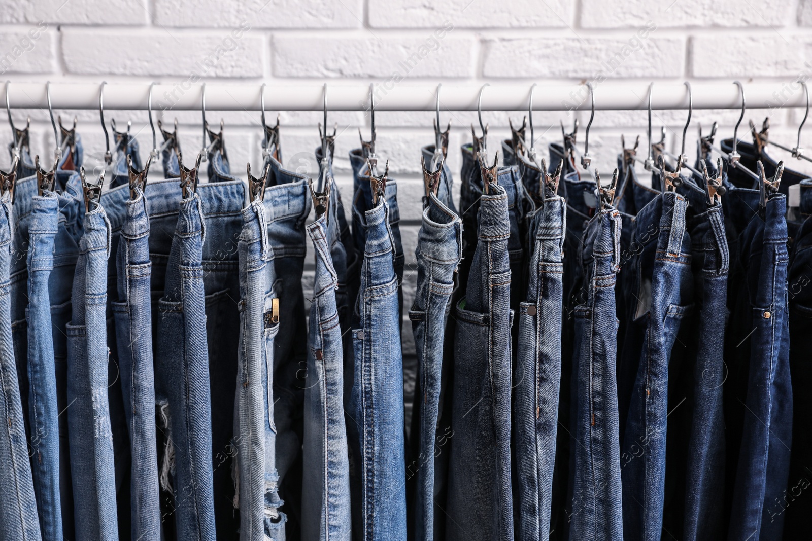 Photo of Rack with stylish jeans near brick wall, closeup