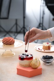 Food stylist creating composition with delicious dessert on table in photo studio, closeup