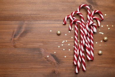 Photo of Sweet Christmas candy canes and festive decor on wooden table, flat lay. Space for text