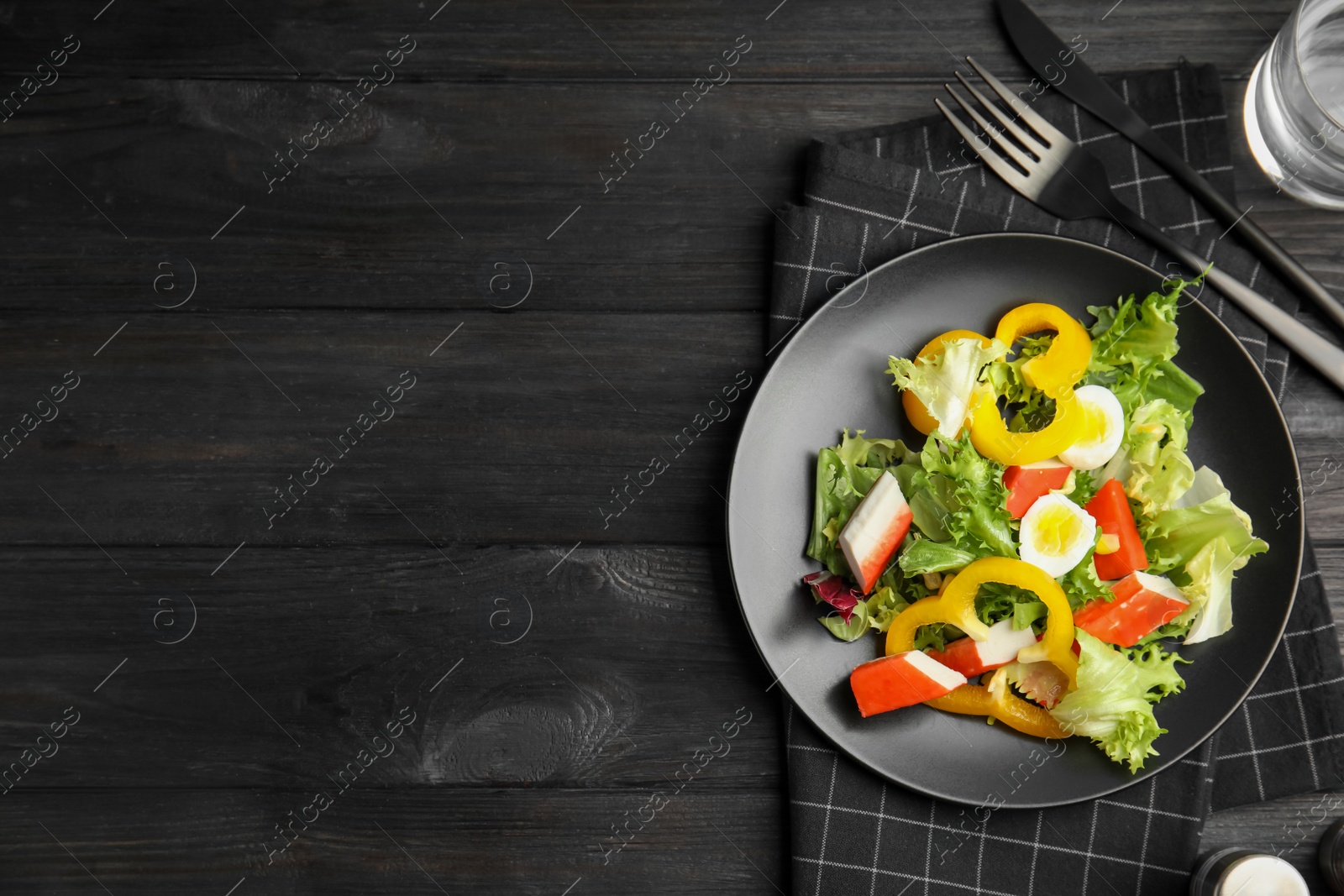 Photo of Salad with crab sticks and lettuce served on black wooden table, flat lay. Space for text