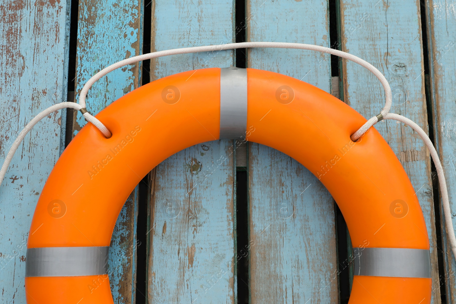 Photo of Orange life buoy on light blue wooden background, top view