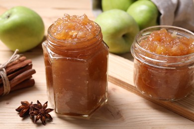 Photo of Delicious apple jam in jars, fresh fruits and spices on wooden table