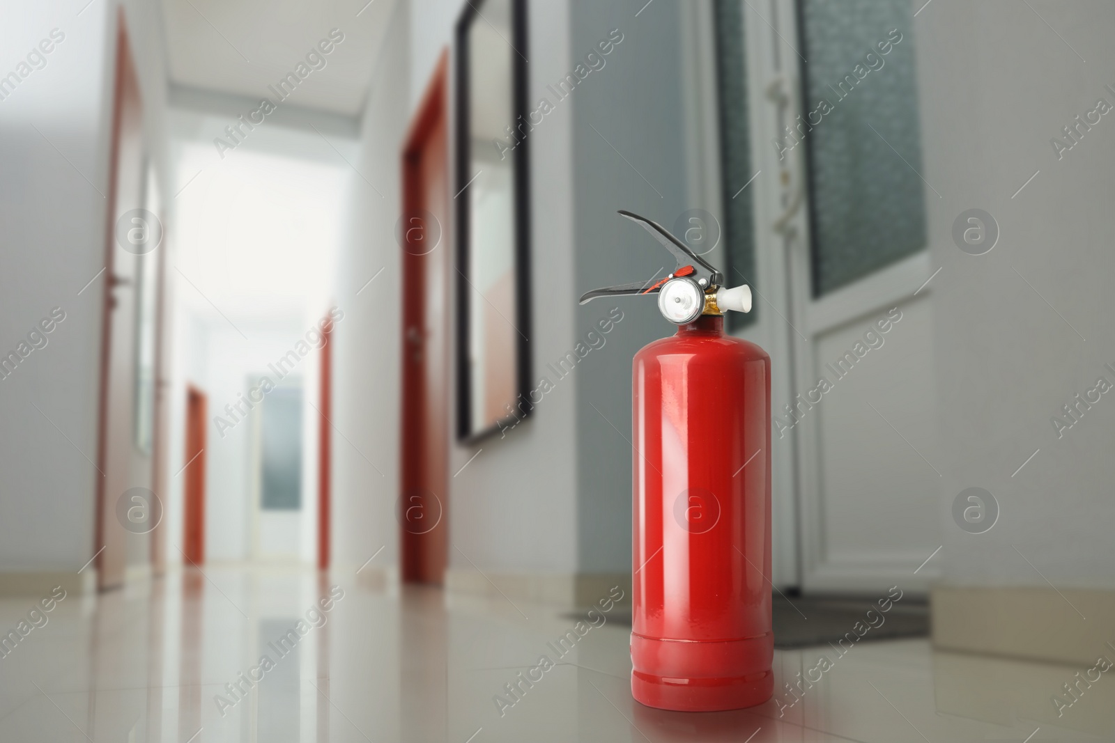 Image of Fire extinguisher on floor in office corridor. Space for text