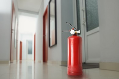 Image of Fire extinguisher on floor in office corridor. Space for text