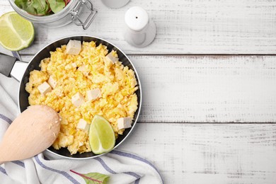 Frying pan with delicious scrambled eggs, tofu and lime on white wooden table, flat lay. Space for text
