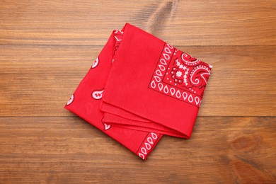 Folded red bandana with paisley pattern on wooden table, top view