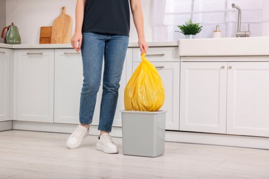 Photo of Woman taking garbage bag out of trash bin in kitchen, closeup