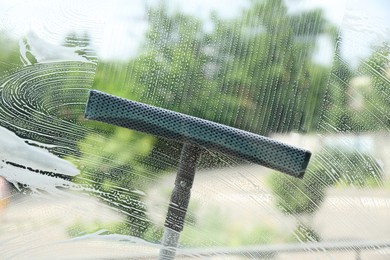 Photo of Washing window with squeegee from outside, view through glass