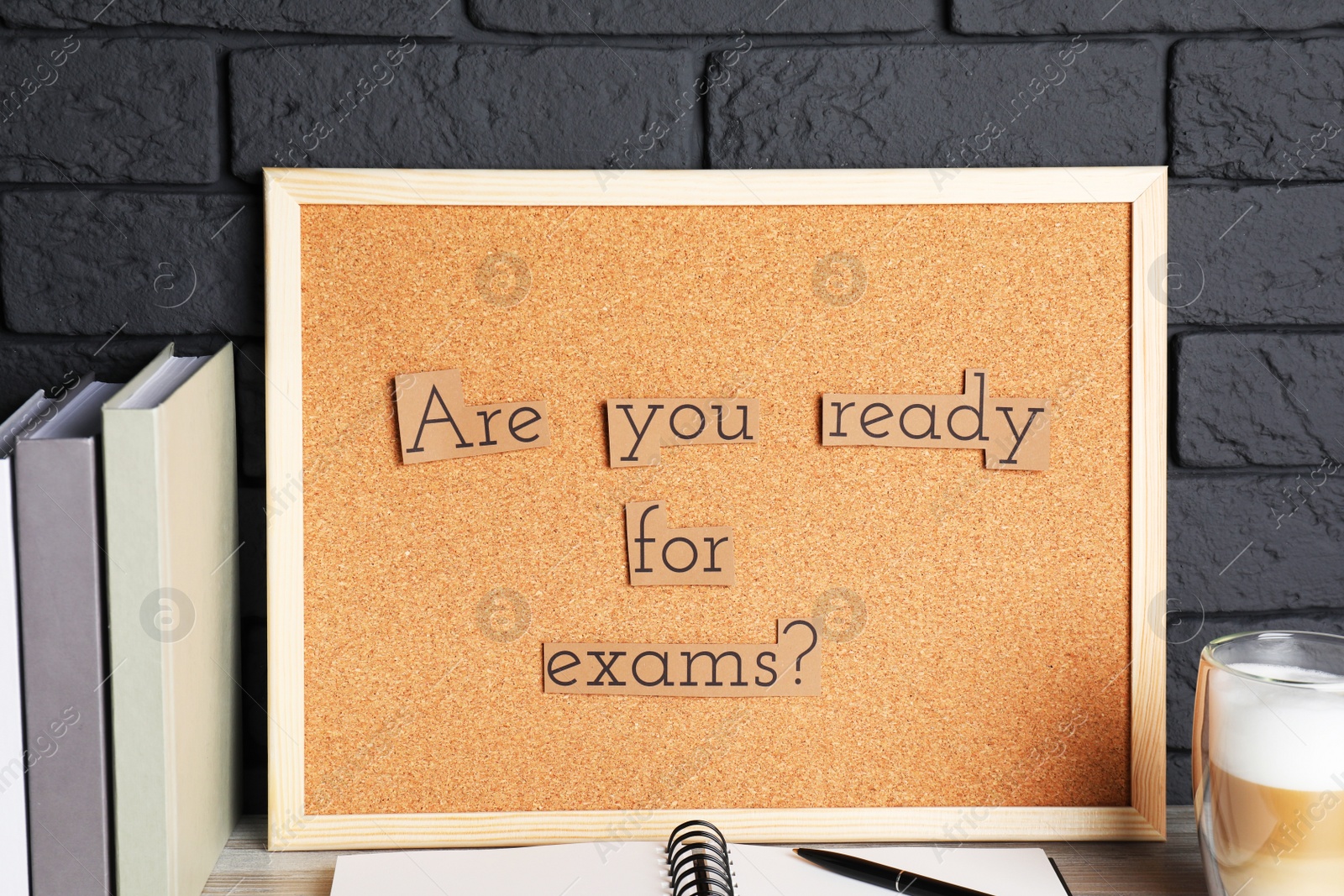 Photo of Cork board with phrase Are You Ready For Exams? on wooden table near black brick wall