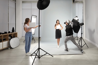 Professional photographer with assistant taking picture of young woman in modern studio