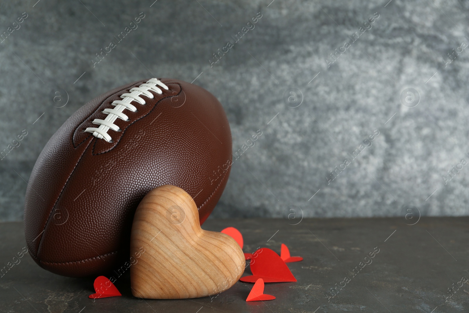 Photo of American football ball and hearts on grey table. Space for text