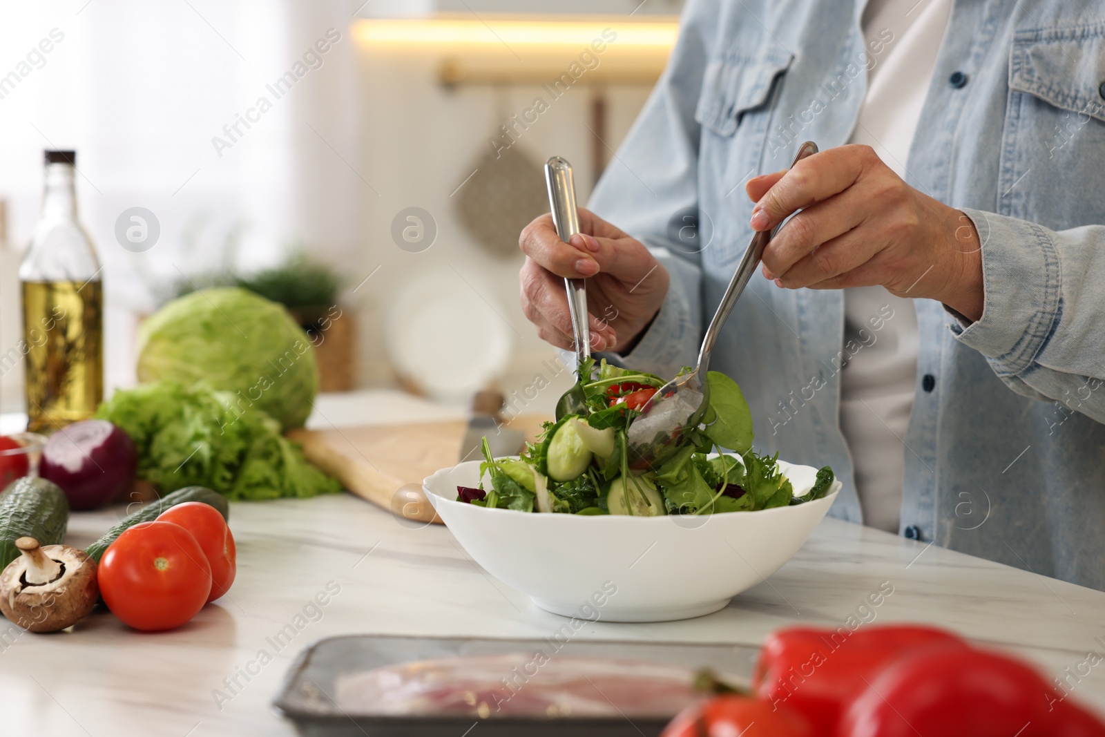 Photo of Woman making salad at white marble table in kitchen, closeup