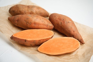 Parchment with cut and whole sweet potatoes on white table, closeup