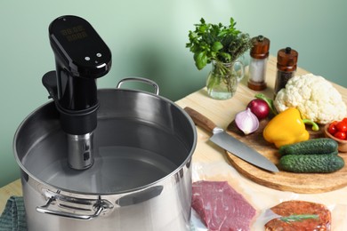 Photo of Pot with sous vide cooker, meat in vacuum packing and other ingredients on wooden table. Thermal immersion circulator