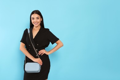 Beautiful young woman with stylish bag on light blue background, space for text