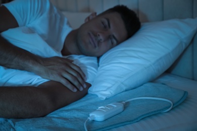 Man sleeping on electric heating pad in bed at night