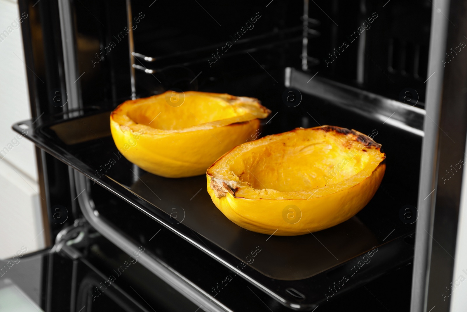 Photo of Baking sheet with halves of cooked spaghetti squash in oven