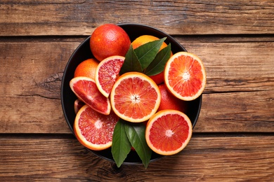 Whole and cut red oranges with green leaves on wooden table, top view