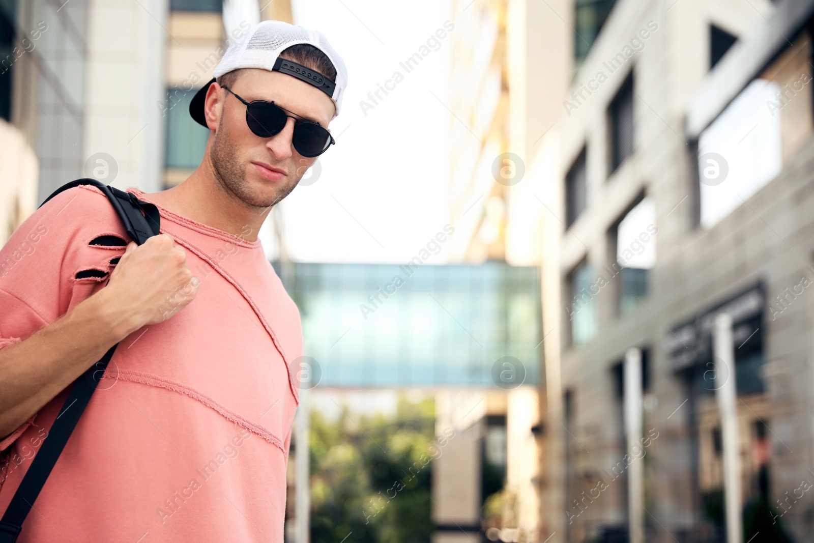 Photo of Handsome young man with stylish sunglasses and backpack on city street, space for text