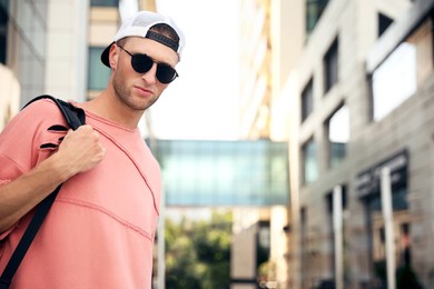 Photo of Handsome young man with stylish sunglasses and backpack on city street, space for text