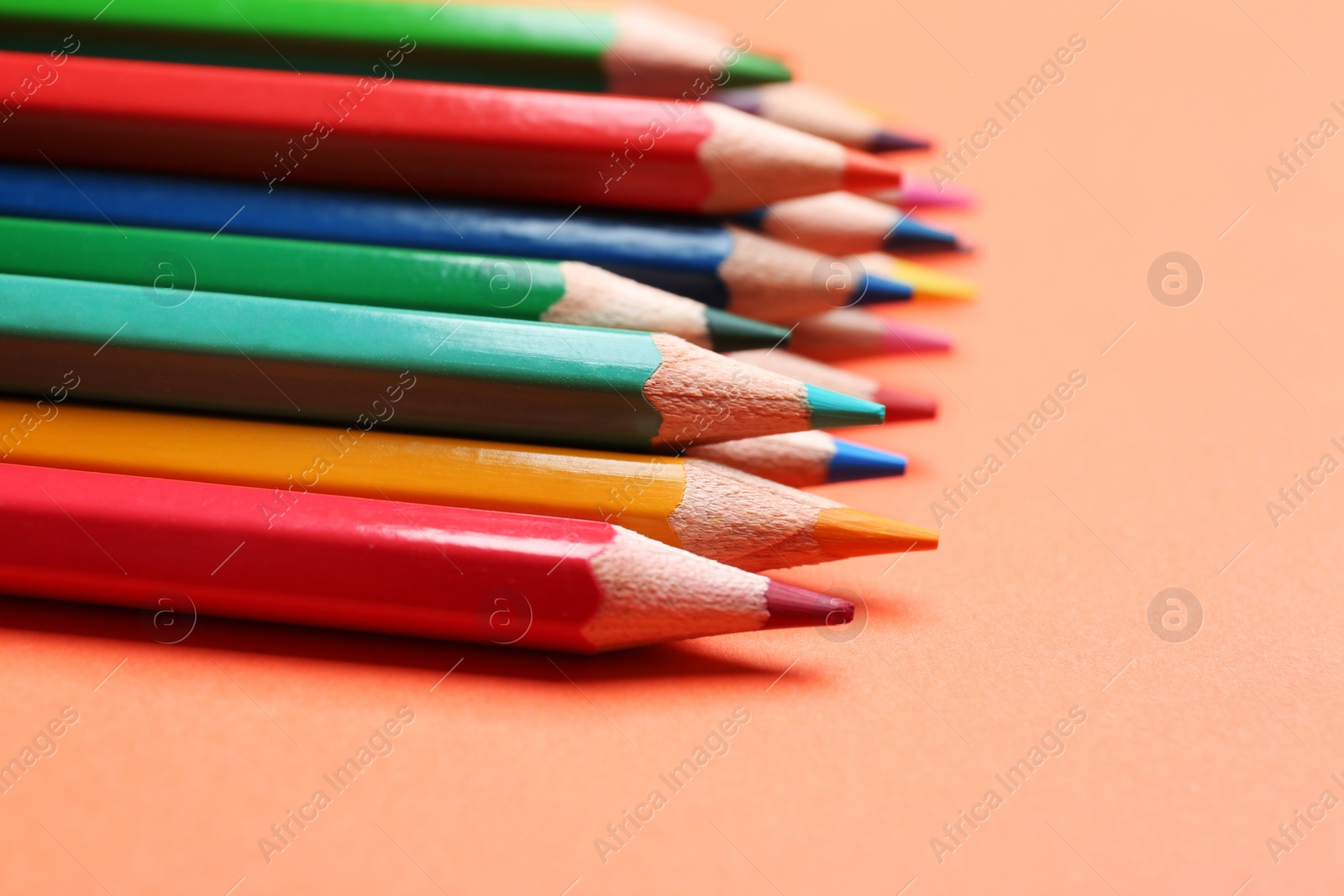 Photo of Different color pencils on coral background, closeup