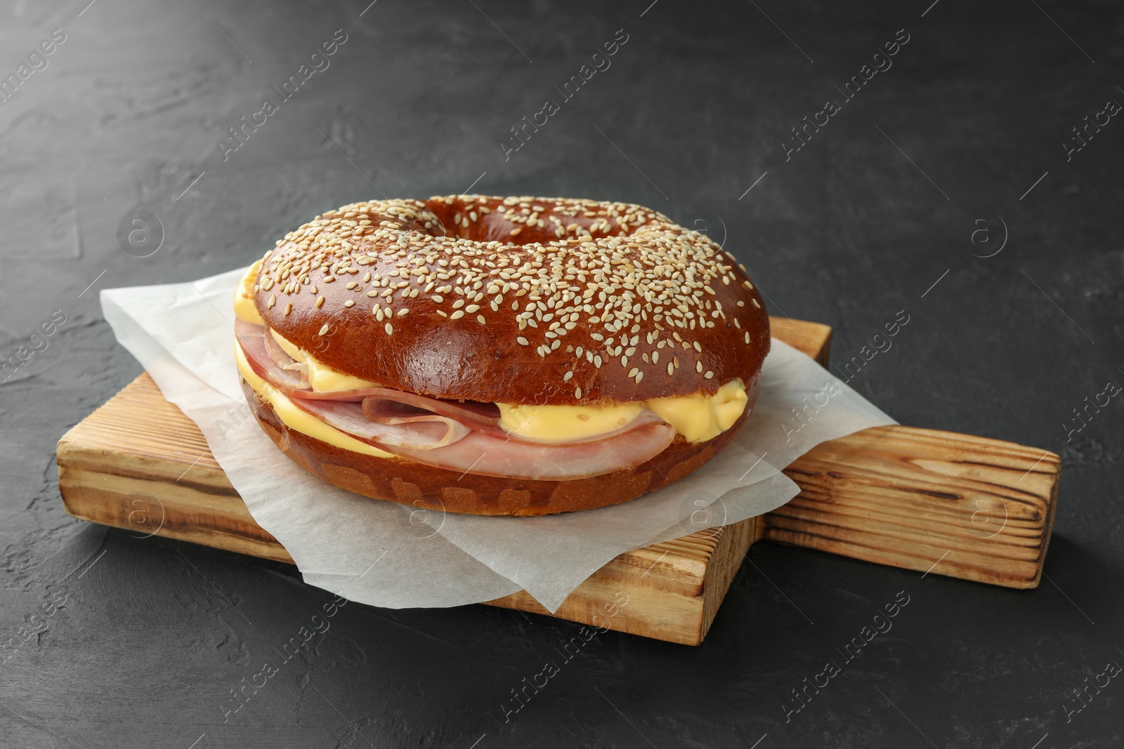 Photo of Delicious bagel with ham and cheese on grey table