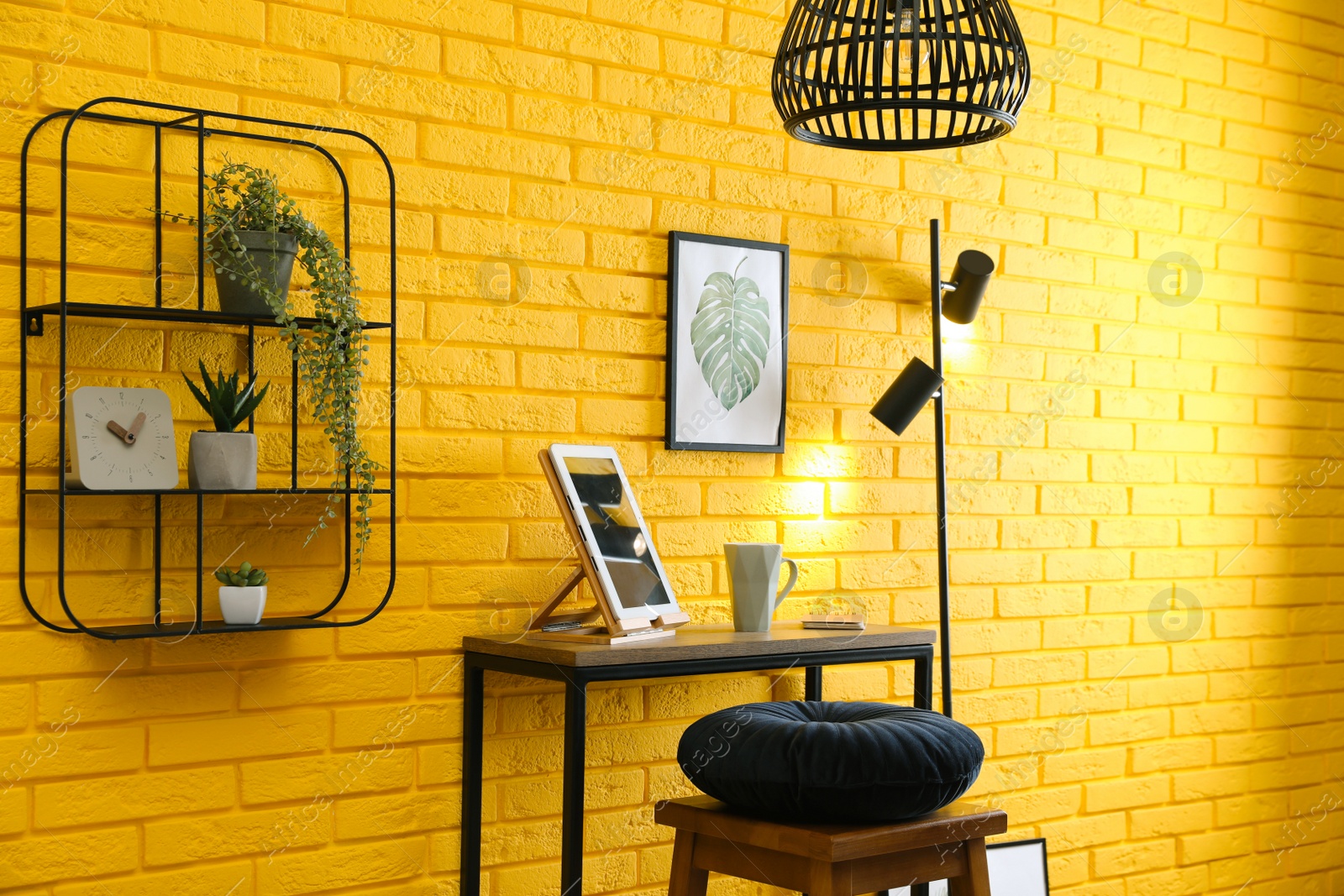 Photo of High wooden table with tablet and stool as stand up workplace near yellow brick wall. Stylish interior