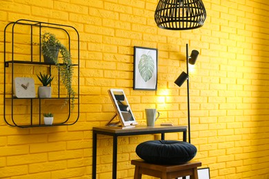 High wooden table with tablet and stool as stand up workplace near yellow brick wall. Stylish interior