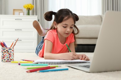 Photo of Little girl drawing on paper with pencil at online lesson indoors. Distance learning