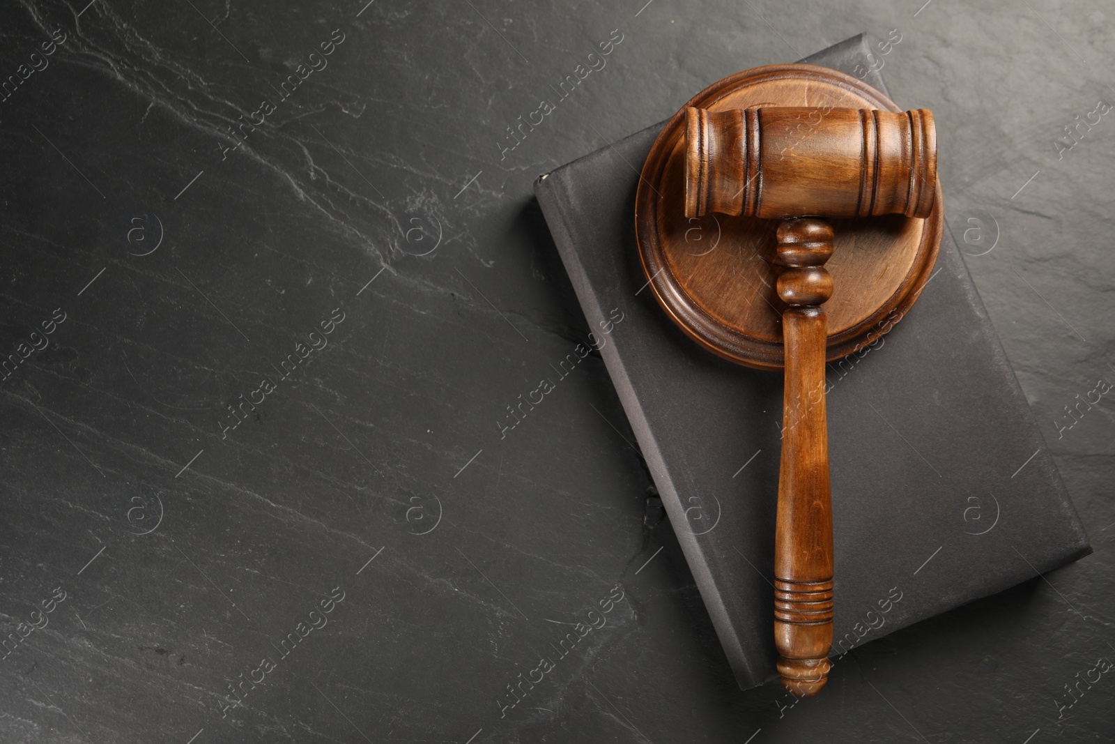 Photo of Wooden gavel, sound block and book on dark textured table, top view. Space for text